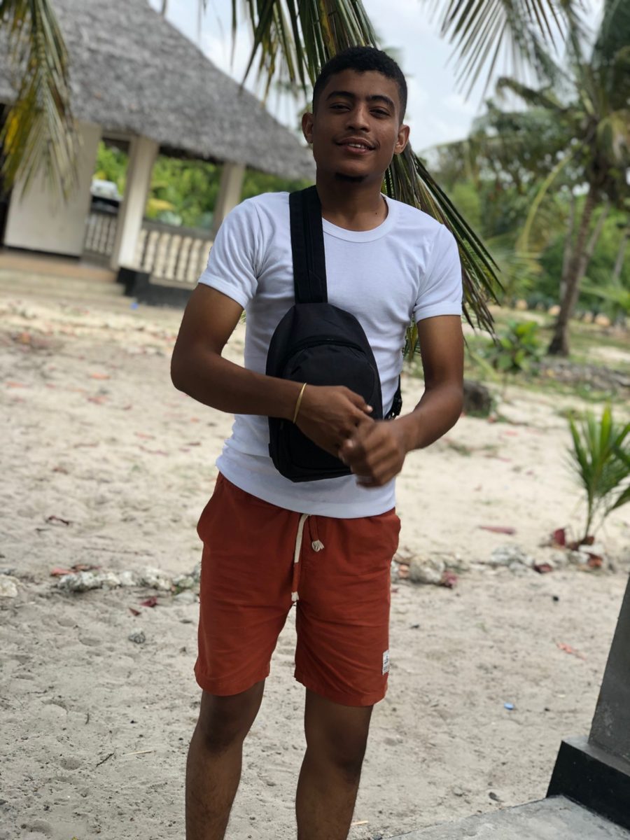 Salem Alawi before his transformation, very slim, standing on a beach in a white T-shirt and shorts